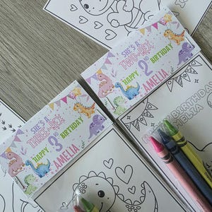 May include: A collection of children's birthday party favors. The favors include coloring pages with dinosaur illustrations and crayon packs. The packaging features text that reads "She's a Two-Rex 2nd Birthday Amelia" and "She's a Three-Rex 3rd Birthday Amelia."