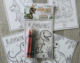 May include: A collection of dinosaur-themed coloring pages and crayons. The pages feature dinosaur illustrations and the name "LOGAN" and the phrase "HAPPY BIRTHDAY LOGAN". One page reads "LOGAN IS 3". The crayons are pink, orange, and green.