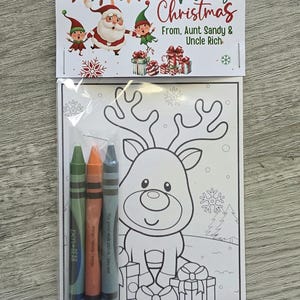 May include: A Christmas-themed coloring book set with three crayons. The top of the package reads "Merry Christmas" with Santa Claus and elves. The coloring page features a reindeer surrounded by presents.
