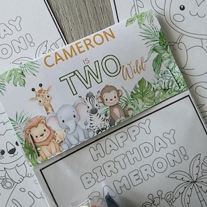 May include: A birthday-themed coloring book set with the text "Cameron is Two Wild." The cover features cartoon animals like a giraffe, lion, elephant, zebra, and monkey. The set includes crayons and a coloring page that says "Happy Birthday Cameron!"