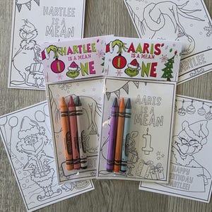 May include: Two clear plastic favor bags containing coloring pages and three crayons each. The header cards feature the text "HARTLEE IS A MEAN ONE" and "AARIS IS A MEAN ONE" with Grinch illustrations. Additional loose coloring pages are scattered around.