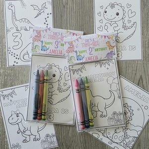 May include: A collection of children's birthday coloring pages featuring dinosaur illustrations. Each page includes the name "Amelia" and the age of the child. Packs of crayons are included with some of the coloring pages.