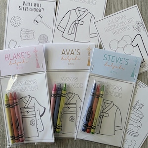 May include: A collection of Doljabi party supplies, including coloring pages with Korean traditional clothing and birthday themes. The set includes crayons and cards with names like "Steve" and "Blake".