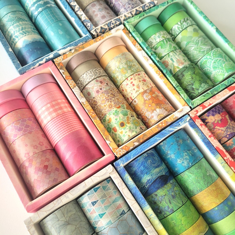 K&ouml;nnte beinhalten: Sortiment an bunten Washi-B&auml;ndern in verschiedenen Mustern und Designs, verpackt in kleinen Schachteln. Die B&auml;nder zeigen florale, geometrische und abstrakte Designs.