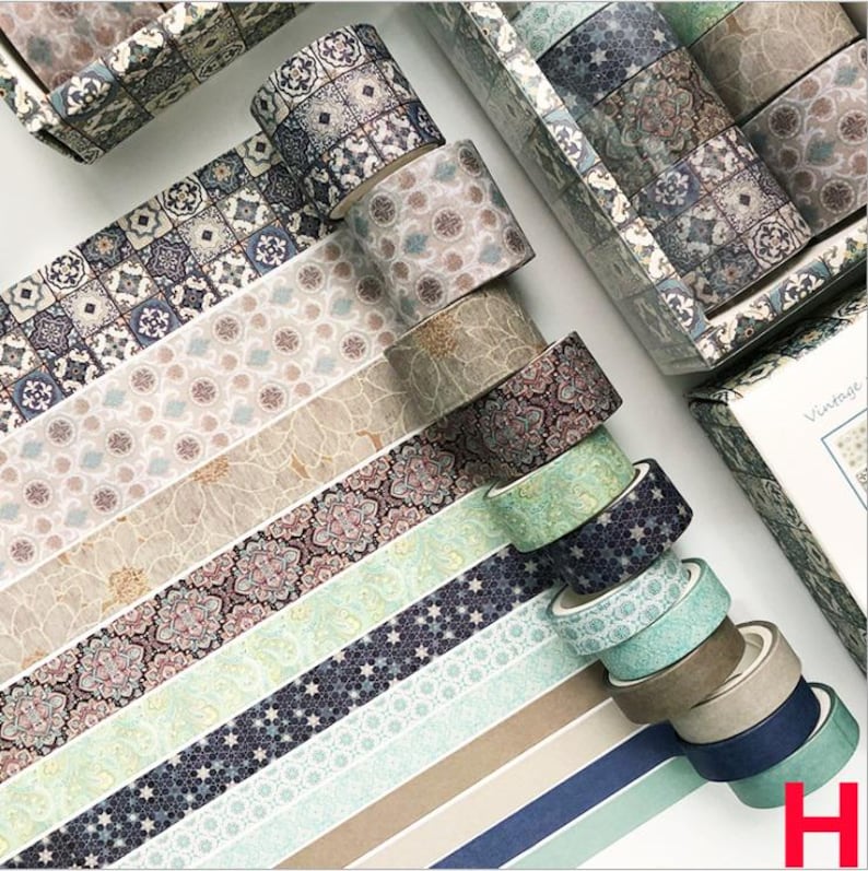 K&ouml;nnte beinhalten: Ein Set aus zehn dekorativen Washi-B&auml;ndern mit verschiedenen Mustern, darunter geometrische, florale und abstrakte Designs. Die B&auml;nder sind in einer Reihe angeordnet, wobei sich die Muster abwechseln. Die B&auml;nder sind alle in Blaut&ouml;nen, Gr&uuml;n, Braun und Wei&szlig; gehalten. Die B&auml;nder sind mit "Vintage" beschriftet.