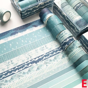 K&ouml;nnte beinhalten: Ein Set mit 10 Washi-B&auml;ndern mit blauen und wei&szlig;en Mustern. Die B&auml;nder zeigen verschiedene Designs, darunter Wellen, Berge und geometrische Formen. Die B&auml;nder sind in einer durchsichtigen Plastikbox mit einem blauen und wei&szlig;en Muster auf dem Deckel verpackt.