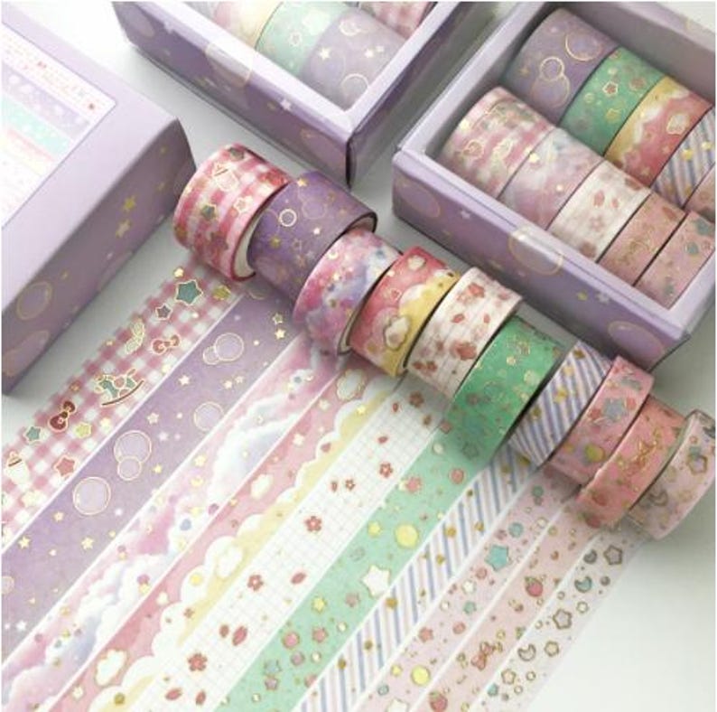 Pu&ograve; includere: Un set di 10 nastri washi colorati con vari motivi, tra cui stelle, nuvole e fiori. I nastri sono decorati con glitter dorati e sono confezionati in una scatola di plastica trasparente con un coperchio viola.