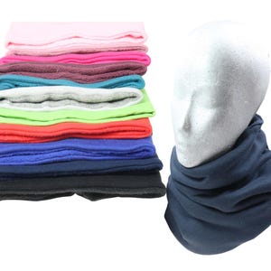 Op de afbeelding: Een stapel fleece hoofdbanden in diverse kleuren, waaronder roze, paars, turquoise, grijs, groen, rood, blauw en zwart. Een marineblauwe fleece nekwarmer wordt getoond op een mannequinhoofd. Deze accessoires zijn ontworpen voor warmte en comfort.