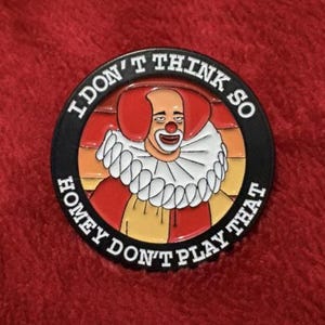 May include: A round, black enamel pin featuring a clown with red hair and a white ruffled collar. The pin has the text "I DON'T THINK SO HOMEY DON'T PLAY THAT" in a circular pattern around the clown image.