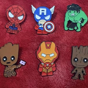 May include: Set of six colorful superhero character pins. Includes Spider-Man, Captain America, Hulk, Groot, Iron Man, and another Groot. Each pin features a detailed design with vibrant colors and a glossy finish. Perfect for fans of comic books and superheroes.