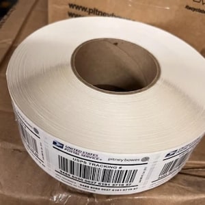 May include: A roll of white shipping labels with a black and white USPS tracking label. The label includes the text "UNITED STATES POSTAL SERVICE." and "pitney bowes". The tracking number is 9485 8090 0027 6191 5719 57.