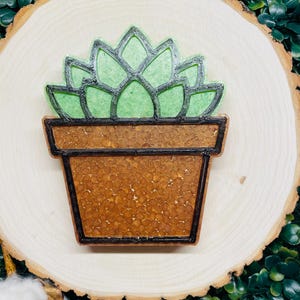 May include: A green succulent plant in a brown pot with a textured surface. The plant and pot are made of resin and are a decorative item.
