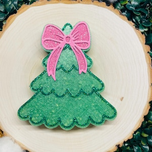 May include: A green glitter Christmas tree ornament with a pink glitter bow on top.