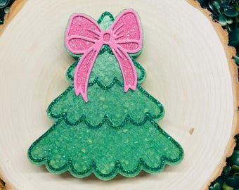 Puede incluir: Un adorno de árbol de Navidad verde con purpurina y un lazo rosa con purpurina en la parte superior.