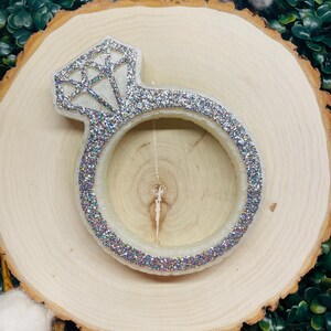 May include: A white ring-shaped candle with a silver glitter finish and a diamond design on top.