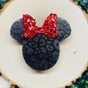 May include: Black and red Minnie Mouse head candle with a leopard print design. The candle has a red glitter bow on top.