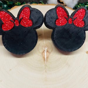 May include: Two black 3D printed Minnie Mouse head ornaments with red glitter bows.