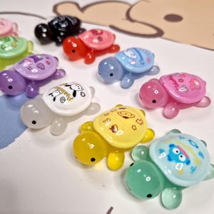 Puede incluir: Diez figuritas de tortugas de colores con diferentes diseños de dibujos animados en sus caparazones. Las tortugas están hechas de un material plástico transparente y tienen un acabado brillante.