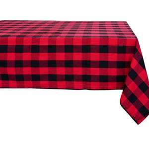 May include: A red and black buffalo plaid tablecloth. The tablecloth is rectangular and covers a table, with a corner hanging off the edge. The pattern consists of large, evenly spaced squares.