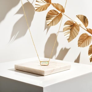 May include: A gold chain necklace with a white opal pendant in a rectangular shape. The necklace is displayed on a white marble surface.