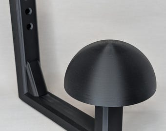 May include: A black plastic 3D printed wall mount with a dome-shaped top. The mount is designed to hold a round object, such as a hat or a helmet.