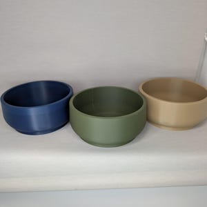 May include: Three small, round bowls in different colours: blue, green, and beige. The bowls are made of a smooth, matt material and are perfect for holding small items.