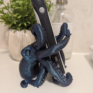 May include: A dark blue 3D printed octopus holding an electric toothbrush. The octopus has a textured surface and is holding the toothbrush in its tentacles.