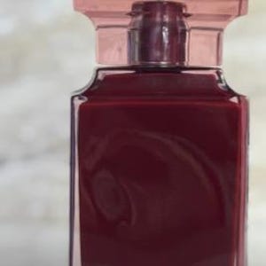 Op de afbeelding: Een rechthoekige glazen fles gevuld met een diepe bordeauxrode vloeistof. De fles heeft een heldere, transparante body en een bijpassende bordeauxrode dop. Het ontwerp van de fles is eenvoudig en elegant, met strakke lijnen en een minimalistische esthetiek.