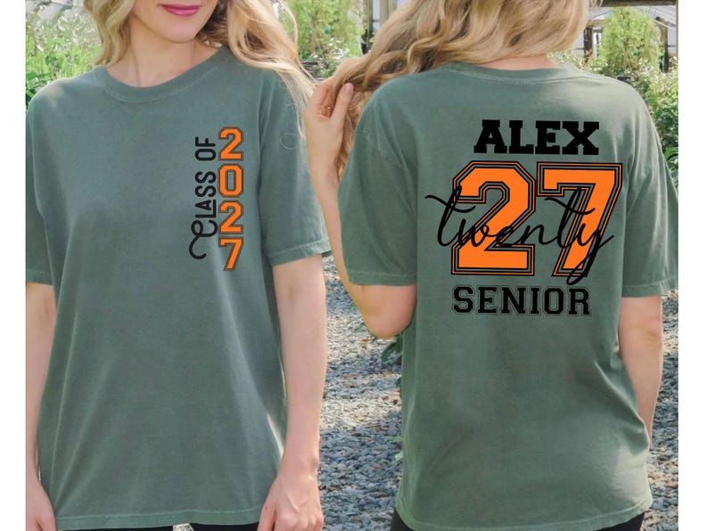 Może przedstawiać: Szałwiowo-zielony t-shirt z pionową pomarańczowo-czarną grafiką na piersi z napisem "CLASS OF 2027". Z tyłu koszulki znajduje się imię "ALEX" w kolorze czarnym, duża pomarańczowa liczba "27" z czarnym obrysem oraz słowo "SENIOR".