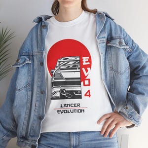 Puede incluir: Camiseta blanca con un diseño de coche, un círculo rojo de fondo y el texto "EVO 4" y "Lancer Evolution". El diseño es una ilustración estilizada. Ideal para los entusiastas de los coches, la camiseta muestra una vista trasera de un coche.