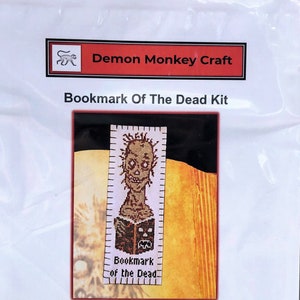 May include: A cross-stitch kit for a bookmark featuring a zombie with the text "Bookmark of the Dead". The kit includes a needle, needle threader, DMC floss, and a pattern.