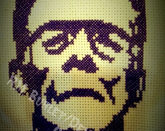 Puede incluir: Patrón de punto de cruz de la cara del monstruo de Frankenstein en morado sobre fondo blanco. El patrón está cosido en tela Aida. El texto "RM BURLEY DEMON MONKEY CRAFT" es visible en la esquina inferior derecha.