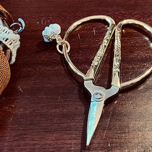 May include: Gold-toned decorative scissors with an ornate design. The scissors have a sharp blade and a small loop at the top.