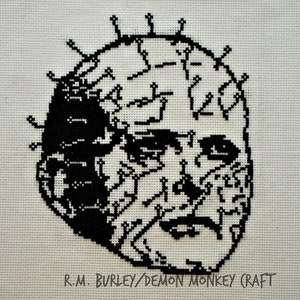 May include: Black and white cross-stitch embroidery of a face with a crown of thorns. The text "R.M. BURLEY/DEMON MONKEY (CRAFT" is at the bottom of the image.