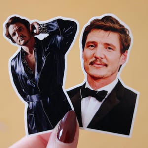 May include: Two stickers of men's faces. The sticker on the left shows a man in a dark blue robe with a white collar. The sticker on the right shows a man in a black tuxedo with a black bow tie.