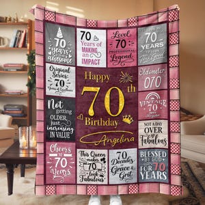 May include: A burgundy and pink patchwork blanket with gold text celebrating a 70th birthday. The blanket features phrases like "Happy 70th Birthday Angelina", "Vintage 70", and "Blessed by God for 70 Years".