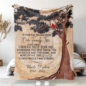 May include: A beige blanket featuring a tree design with a red cardinal. The text reads "A limb has fallen from our family tree... Uncle Dylan 1952-2025". The blanket has a wood grain background.