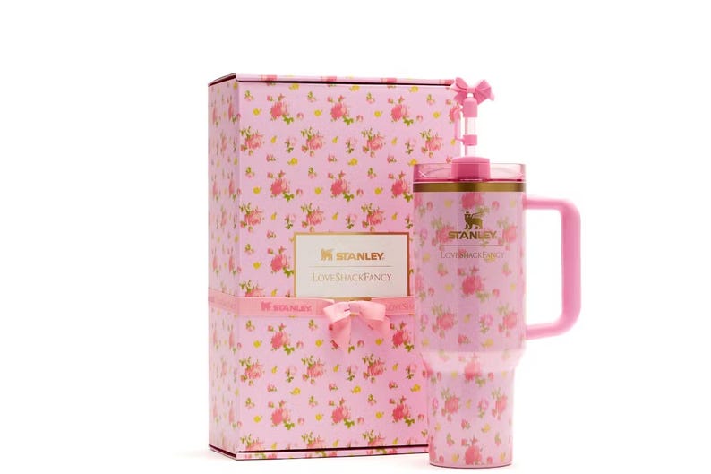 May include: A pink Stanley tumbler with a floral pattern, a matching handle, a lid, and a straw topped with a small pink bow. The tumbler is displayed next to a rectangular gift box featuring the same floral print, a pink ribbon, and the Stanley LoveShackFancy logo.