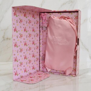 May include: A pink floral patterned box containing a light pink drawstring pouch with the Stanley and LoveShackFancy logos printed in white, alongside a clear straw featuring a small pink bow detail at the top, presented in a gift set.