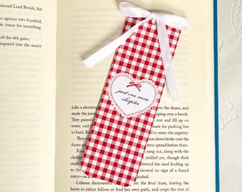 May include: Red and white gingham bookmark with a white ribbon, resting in an open book. The bookmark has a heart-shaped embellishment with the text "just one more chapter". A charming accessory for book lovers.
