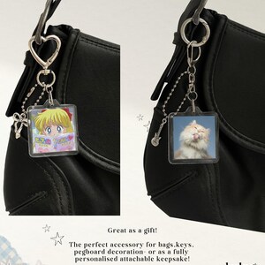 May include: Two square acrylic keychains attached to black bags. One features an anime character reading a book, the other a fluffy cat licking its nose. Both include silver-toned heart or guitar charms and ball chains with metal clasps.