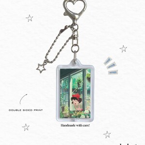 May include: A rectangular keychain with a heart-shaped clasp and a star charm. The keychain features a double-sided print of an anime scene with a girl in a red bow. Text on the keychain reads "Handmade with care!"