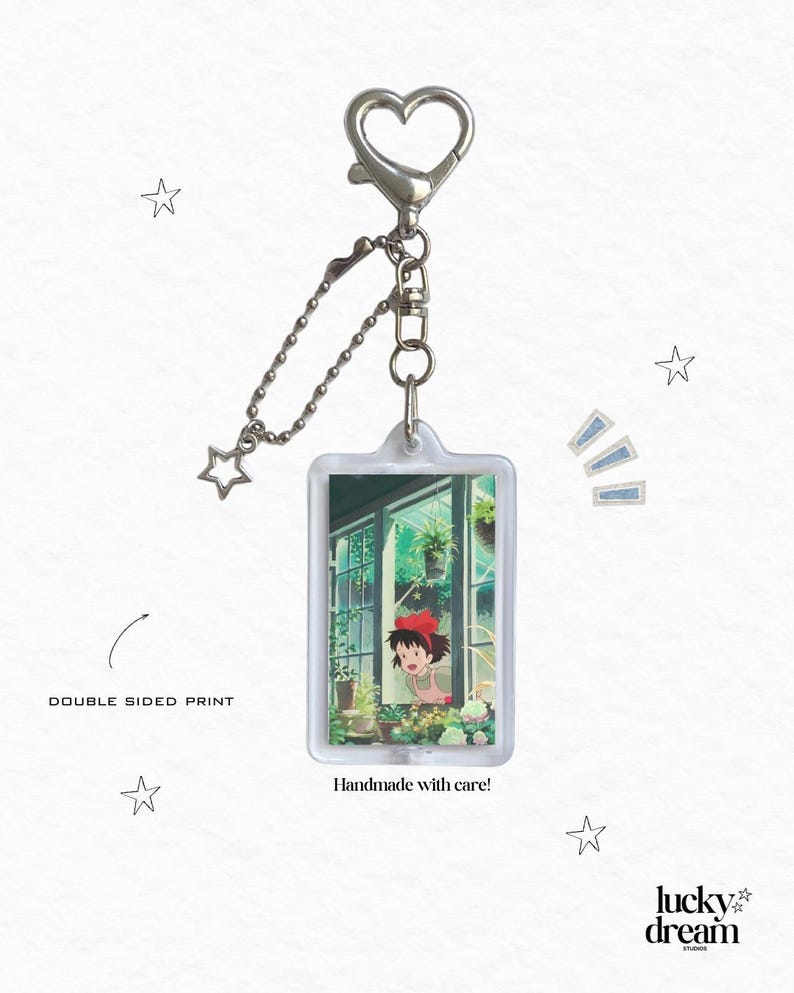May include: A rectangular keychain with a heart-shaped clasp and a star charm. The keychain features a double-sided print of an anime scene with a girl in a red bow. Text on the keychain reads "Handmade with care!"