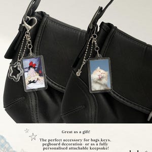 May include: Two black bags with attached keychains. One keychain has a star-shaped charm and a rectangular image of an anime character. The other keychain has a guitar charm and a rectangular image of a cat. Text reads: "Great as a gift!"