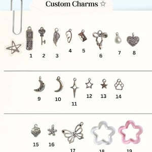 May include: A collection of nineteen numbered metal and resin charms labeled Custom Charms. The set includes shapes like a flip phone, key, wing, envelope, bow, pearl, heart, moon, star, paw print, strawberry, flower, butterfly, and star-shaped rings.
