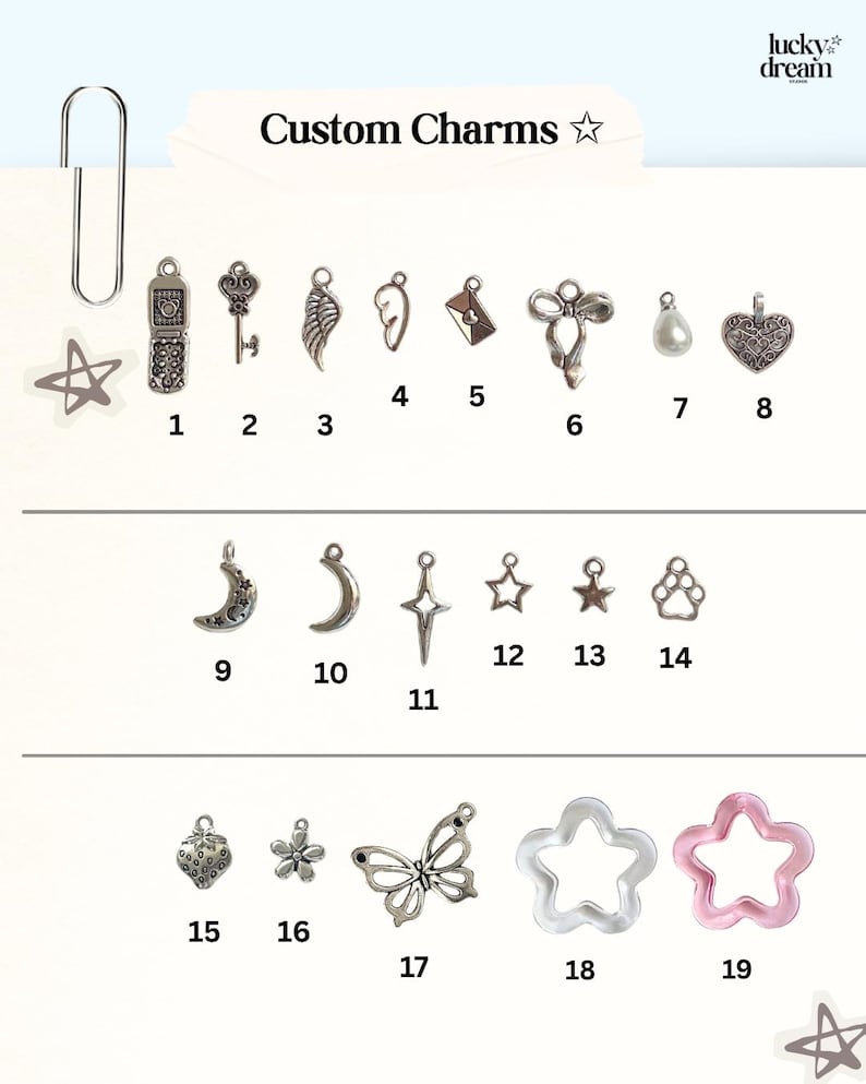 May include: A collection of nineteen numbered metal and resin charms labeled Custom Charms. The set includes shapes like a flip phone, key, wing, envelope, bow, pearl, heart, moon, star, paw print, strawberry, flower, butterfly, and star-shaped rings.