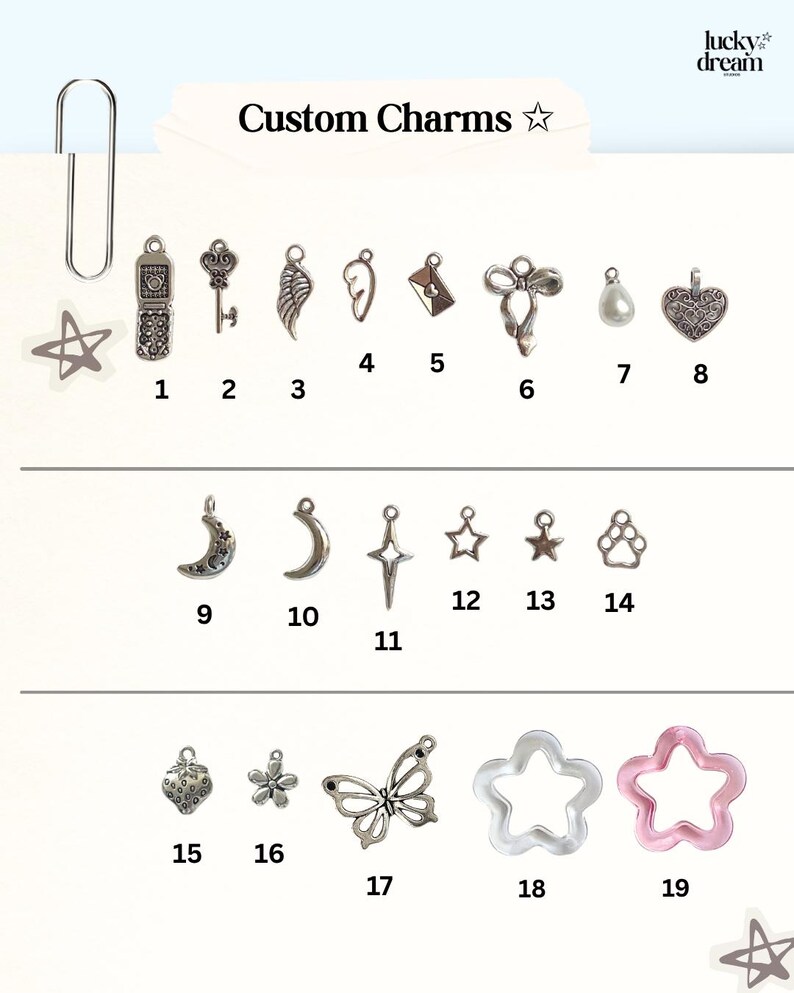 May include: A collection of nineteen numbered metal and resin charms labeled Custom Charms. The set includes shapes like a flip phone, key, wing, envelope, bow, pearl, heart, moon, star, paw print, strawberry, flower, butterfly, and star-shaped rings.
