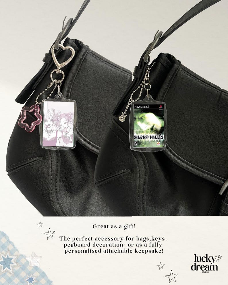 May include: Two black shoulder bags featuring rectangular clear plastic keychains. One keychain displays a manga-style illustration of two characters, while the other shows the Silent Hill 2 PlayStation 2 game cover. Both have metal hardware.