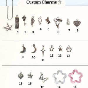May include: A collection of custom charms, including a star, a flip phone, a key, wings, an envelope, a bow, a pearl, a heart, a crescent moon, a star, a paw print, a flower, a butterfly, and star shapes. The text "Custom Charms" is visible.