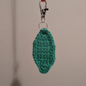 May include: A teal green crocheted leaf charm attached to a silver key chain with a red rubber band.